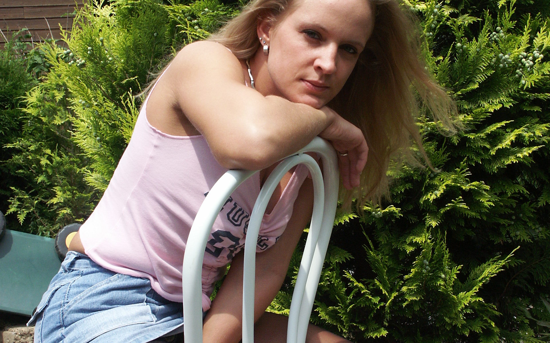 Junge Blondine sitzt im Top auf Stuhl im Garten